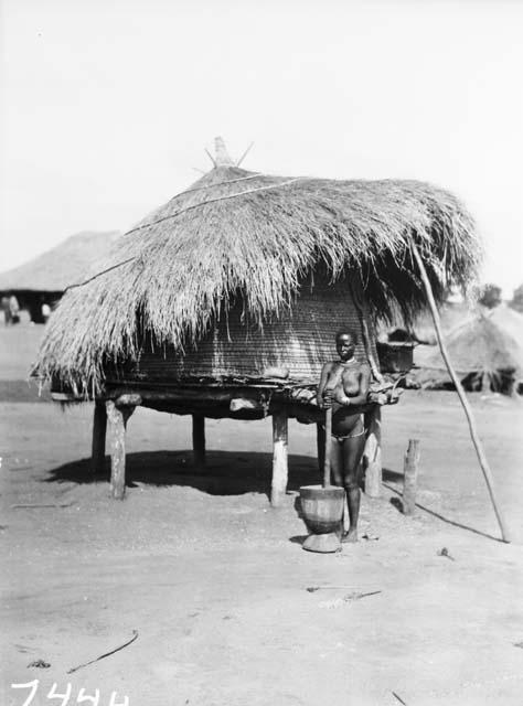 Woman standing with mortar and pestle in front of granary