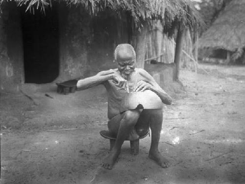 Old man on stool fixing cracked calabash, bowl or food container