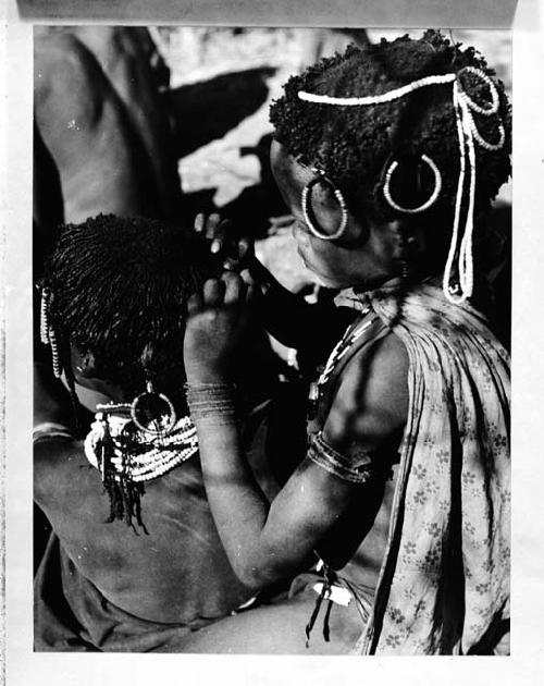 Girl looking for lice in the hair of a smaller child (copy negative)