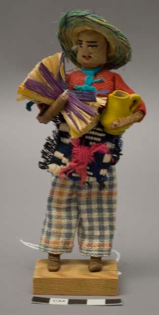 Doll, man with clay vessel and wood bundle, affixed to stand