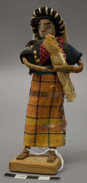 Doll, woman with plant fiber bundle, affixed to stand