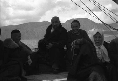 Group of pilgrims, sitting on boat, mountains on far side of water