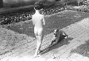 David Lattimore, naked on stone pathway, dog lying in path in front of him