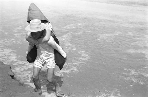 Man carrying Agnes Jaffe on his back across river