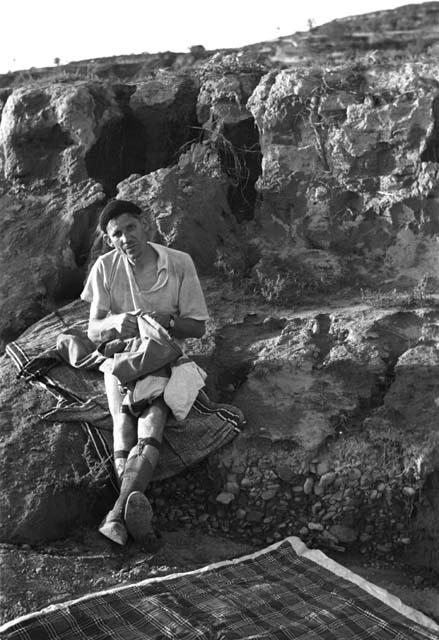 T. A. Bisson in underwear sitting on rock with clothing in his lap