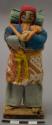 Doll, man with cloth bag and bundle on back, affixed to stand