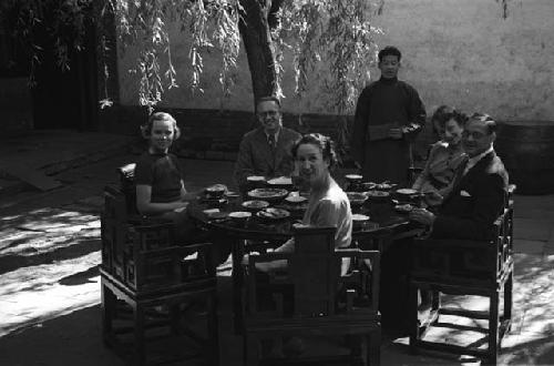 Eleanor Lattimore, two women and one man all seated at round table in courtyard