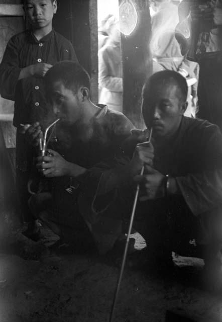 Two men with closely-cropped hair sitting and smoking pipes