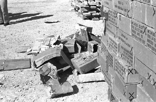 Boxes piled together and some destroyed lying over sand