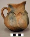 Pottery pitcher, unpainted, with punctated and raised design around neck.