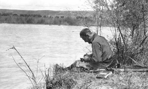 Owen Lattimore (?) sitting on a riverbank writing