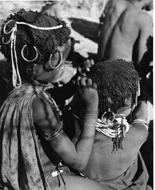 "Grooming & haircuts": Girl looking for lice in the hair of a smaller child (print is a cropped image)