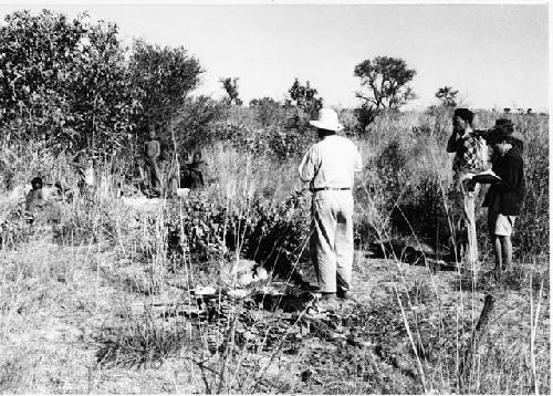 Group of people sitting, with Lorna Marshall, Laurence Marshall, John Marshall, and Elizabeth Marshall Thomas (taking notes) standing to the side