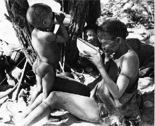 DaSi!Na and N!whakwe drinking, with Tsekue reclining in the background