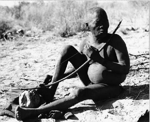 Oukwane seated, playing a bow under a tree