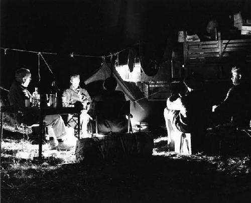 Laurence Marshall and John Marshall with other expedition members sitting by the fire at night