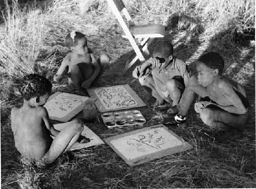 "Paintings, drawing and modelling": Four boys painting with Western materials, including /Gishay ("Old Gau's" son), with his foot bandaged, and Tsamgao (≠Toma's son), wearing a feather in his hair