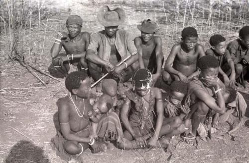 Unidentified Ju/'hoan man, Herero man wearing a hat, unidentified Ju/'hoan man (all three visiting from Kai Kai), ≠Toma, Tsamgao (his son), and /Gunda (husband of N!ai) sitting in the back row; and  !Ungka (≠Toma's sister from Kai Kai) with Sa≠gai and ≠Kham (her two children), an unidentified girl, !Ungka (Norna) (daughter of ≠Toma and !U), and !U with Di//kaho (her baby) sitting in the front row