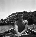 Man holding oars in boat with rock formation/island in background