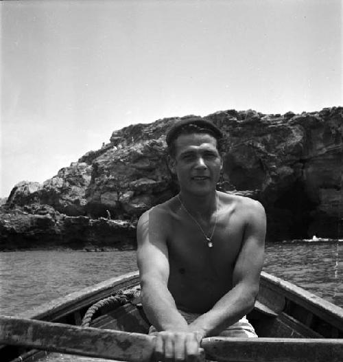 Man holding oars in boat with rock formation/island in background