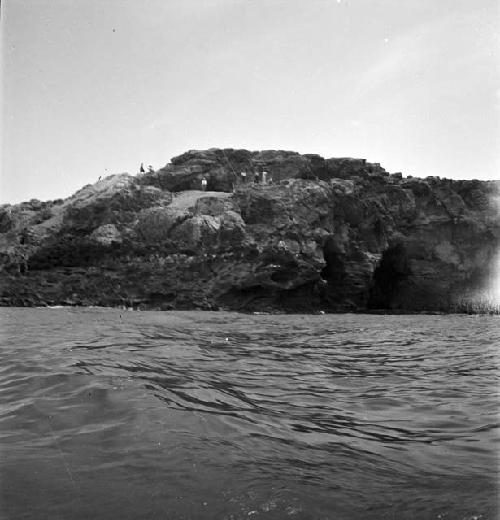 Several people on rock formation/island (picture taken from water)