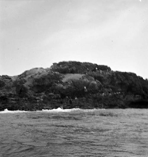 Several people on rock formation/island (picture taken from water)