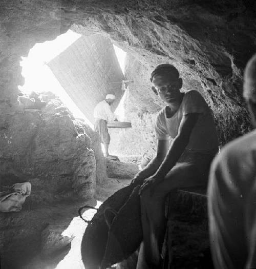 Man sits in foreground while another works in background