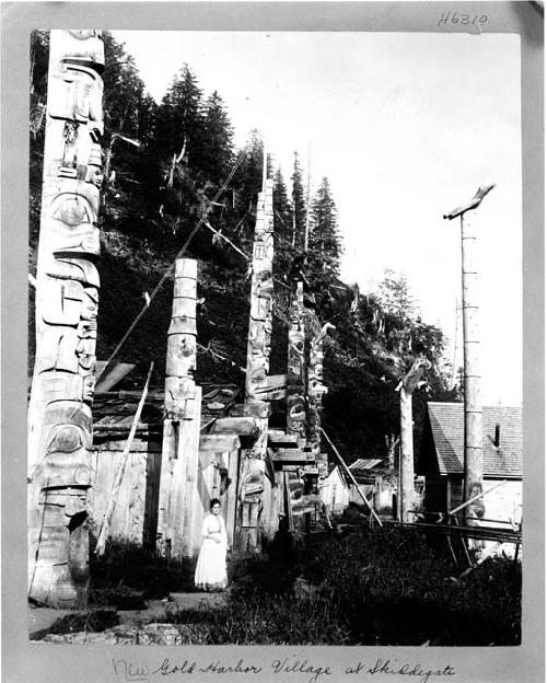 Woman standing in village along row of totem poles