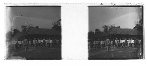 stereo glass slides; man in front of group of men, hut in background