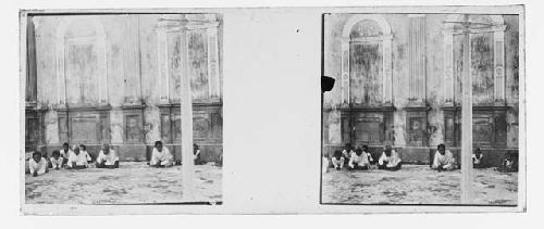 stereo glass slides; men seated cross legged next to building