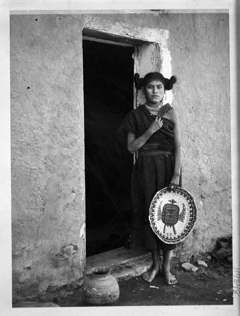 Hopi woman standing in a doorway and holding a basket