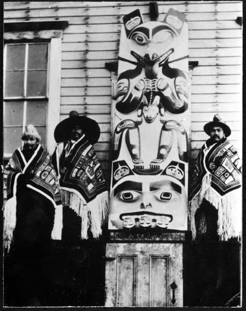 Haida standing next to totem pole