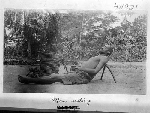 Man lying on ground, leaning against backrest