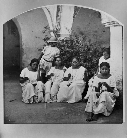 Seven women, seated, with spindles