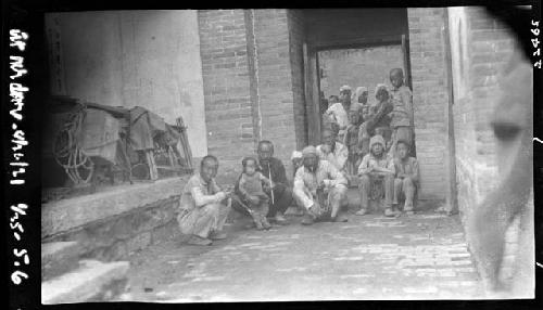 Men and children sit outside building