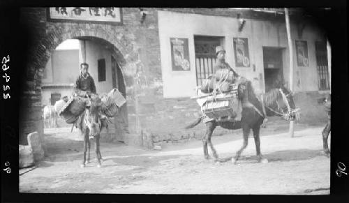 Men ride horses loaded with cargo through a gate