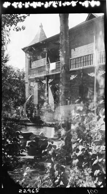 Woman standing with umbrella, superimposed over shot of building and foliage