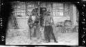 Two men with weapons stand outside building