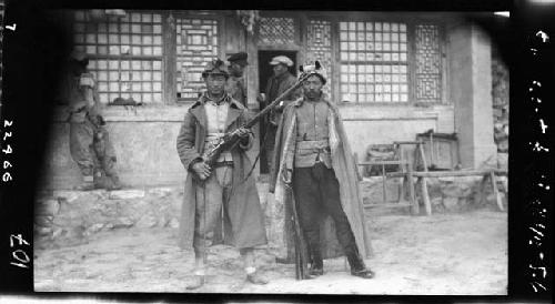 Two men with weapons stand outside building
