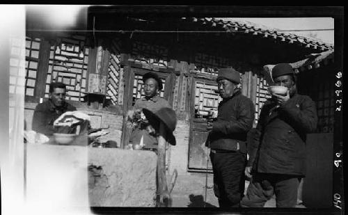 Men standing outside, eating and drinking