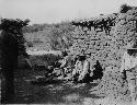 3 people in yard of mud brick house