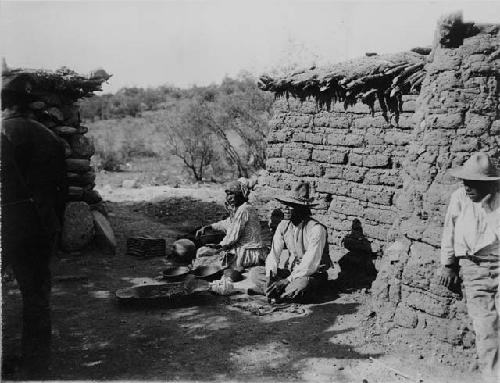 3 people in yard of mud brick house