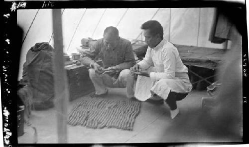 Men crouch over work inside tent