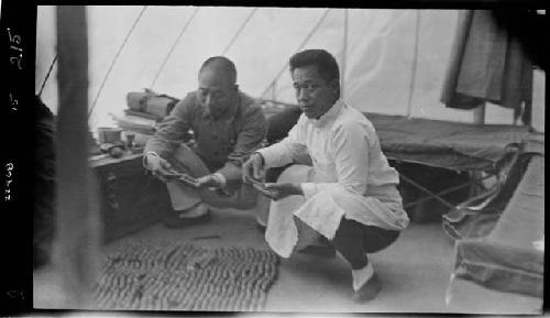 Men crouch over work inside tent