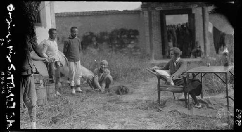 Men stand outside speaking with woman seated at table