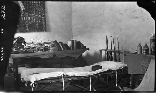 Interior of room, with cot and table full of books