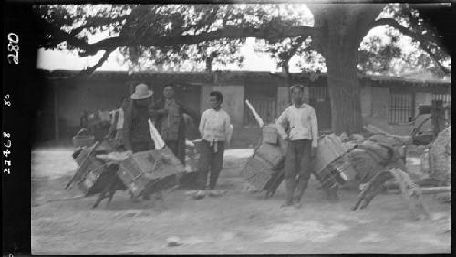 Men stand outside with boxes on carts