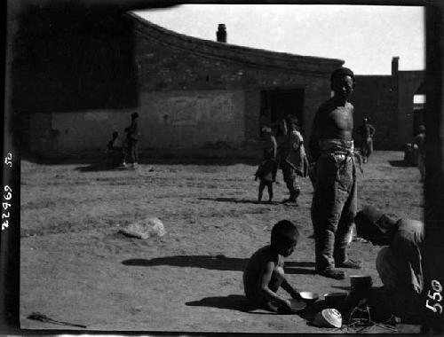 Adults and children standing and sitting on ground outside building