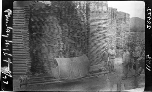 People stand in front of large stacks of materials