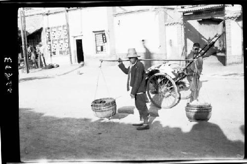 Person carrying baskets on stick over shoulder